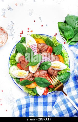 Salade Périgord avec foie de poulet rôti, tomates rouges, concombres, œufs durs, laitue et épinards. Arrière-plan de la table de cuisine noire, vue du dessus Banque D'Images