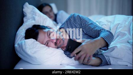 Young Man Using Cellphone pendant que sa femme assis sur le lit la nuit Banque D'Images