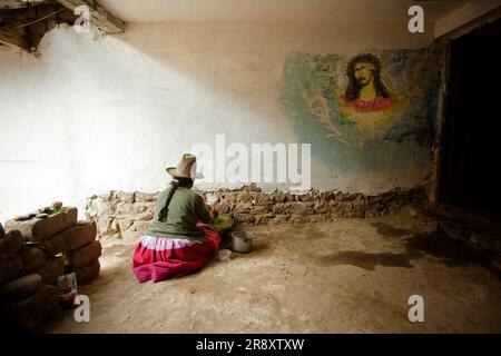 Une femme péruvienne assise sur le sol dans sa maison à côté d'un mur avec une peinture religieuse. Huaraz, Pérou. Banque D'Images