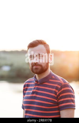 homme d'âge moyen avec une barbe dans un t-shirt aux rayons du soleil Banque D'Images