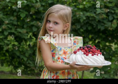 Portrait d'adorable petite fille en robe florale d'été tenant plateau avec gâteau Pavlova Banque D'Images