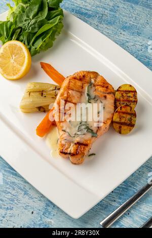 Saumon grillé en sauce avec légumes et pommes de terre sur une assiette en porcelaine blanche Banque D'Images