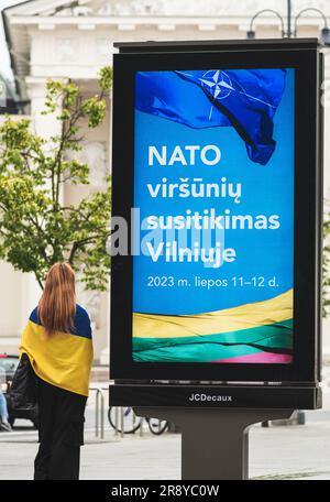 Bannière publicitaire informant sur le prochain sommet de l'OTAN 2023 dans le centre de Vilnius, capitale de la Lituanie, avec une jeune fille drapeau de l'Ukraine marchant Banque D'Images