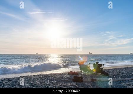 Vue de deux personnes en chaise sur la plage du Rialto sur la partie côtière du parc national olympique, WA, États-Unis avec une lumière de lentille de fin d'après-midi basse et grand Banque D'Images