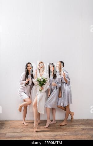 douche de mariée, femmes multiculturelles tenant des verres avec champagne, mariée avec bouquet montrant son anneau d'engagement, demoiselles mariées, diversité, positivité, Banque D'Images