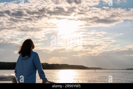 Femme se tenant sur le front de mer en face de la rivière et profitant du coucher du soleil. Bien-être mental, tranquillité dans la nature. Banque D'Images