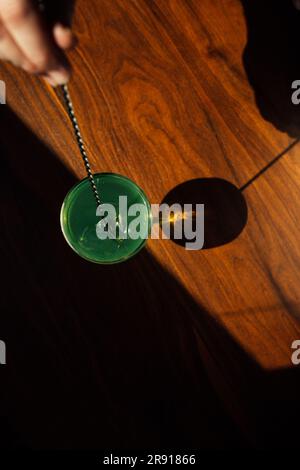 brasser à la main l'absinthe verte dans un verre coupé avec une cuillère à barres argentées sur une table en bois au soleil Banque D'Images