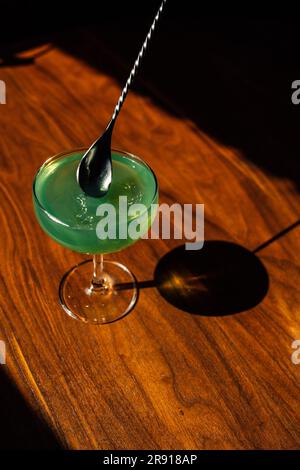 en remuant l'absinthe verte dans un verre coupé avec une cuillère à barres argentées sur une table en bois au soleil Banque D'Images