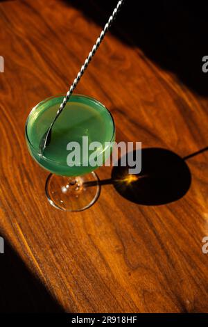 en remuant l'absinthe verte dans un verre coupé avec une cuillère à barres argentées sur une table en bois au soleil Banque D'Images