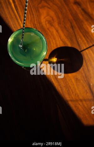 en remuant l'absinthe verte dans un verre coupé avec une cuillère à barres argentées sur une table en bois au soleil Banque D'Images