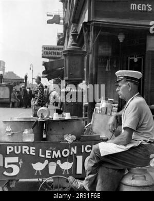 États-Unis: c. 1950 Un vendeur de glace de citron est assis près de son chariot. Banque D'Images