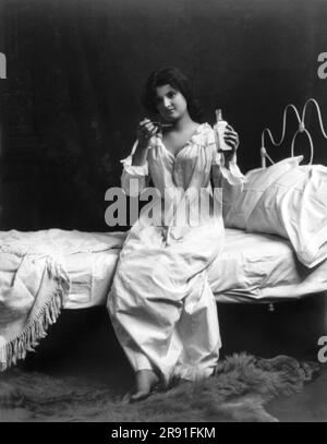 États-Unis: c. 1900 Une jeune femme assise sur un lit prenant une cuillerée de médecine. Banque D'Images