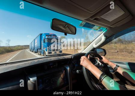 Une femme conduit une voiture le long d'une autoroute australienne car un grand train routier vient dans la direction opposée Banque D'Images