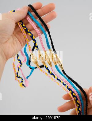 Un gros plan de la main d'une personne tenant plusieurs bracelets d'amitié tissés colorés décorés de breloques en or Banque D'Images