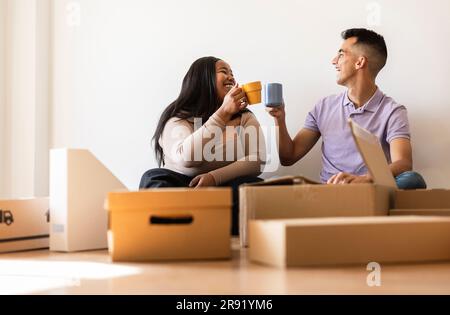 Couple souriant appréciant le café assis près des boîtes en carton dans la nouvelle maison Banque D'Images
