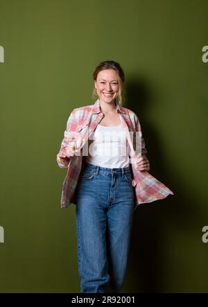 Jeune femme souriante portant une chemise à carreaux debout devant le mur vert Banque D'Images