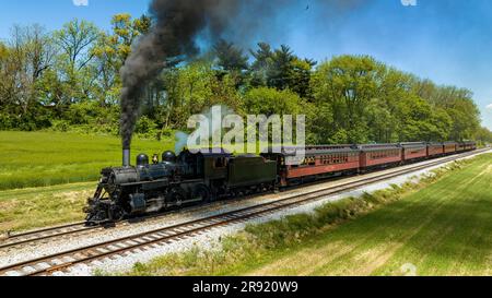 Une vue aérienne du côté d'une locomotive à vapeur antique et d'un autocar de passager s'est arrêtée et a soufflé de la fumée et de la vapeur, en attendant que les passagers montent à bord lors d'une Sunny Spring Day Banque D'Images