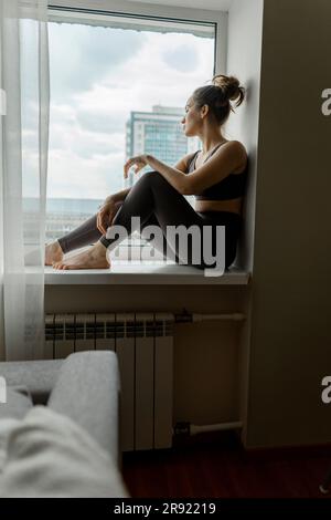 Une femme assise sur un rebord de fenêtre à la maison Banque D'Images