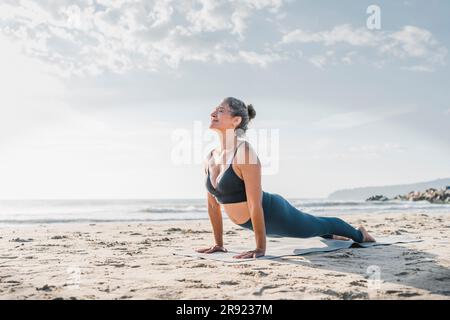 Femme pratiquant le yoga avec cobra pose devant le ciel à la plage Banque D'Images