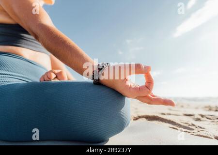 Femme portant un bracelet pratiquant la position de Lotus à la plage Banque D'Images