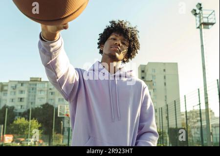 Athlète confiant portant un sweat à capuche violet tenant le basket-ball sur le terrain de sport Banque D'Images