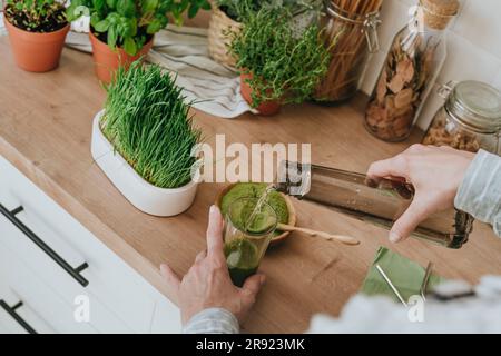 Femme ajoutant de l'eau dans le jus de wheatgrass à la maison Banque D'Images