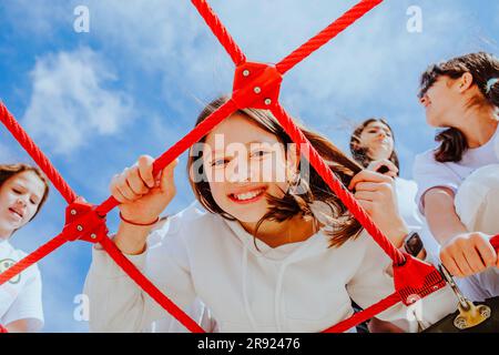 Bonne adolescente avec des amis jouant à la jungle gym à l'aire de jeux Banque D'Images