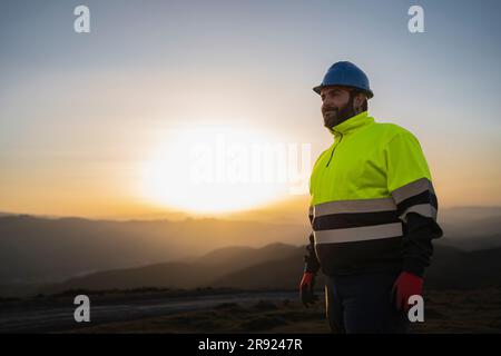 Ingénieur souriant portant un costume réfléchissant au coucher du soleil Banque D'Images