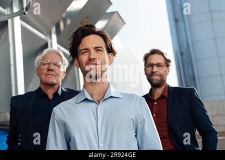 Jeune homme d'affaires avec des collègues debout devant la machinerie Banque D'Images