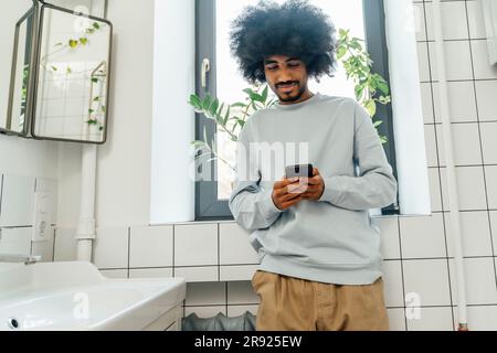 L'homme à l'aide de téléphone mobile dans la salle de bains à la maison Banque D'Images