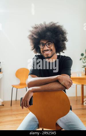 Jeune homme souriant assis sur une chaise à la maison Banque D'Images