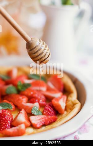 Miel versé sur la petite crêpe hollandaise avec des fraises et de la menthe Banque D'Images