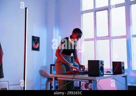 Jeune DJ mélangeant de la musique avec un mélangeur audio à la maison Banque D'Images