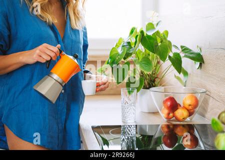 Femme qui verse du café dans la marmite Moka dans la cuisine à la maison Banque D'Images