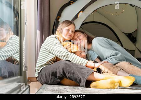 Femme souriante avec son fils et sa fille embrassant le chien à la maison Banque D'Images