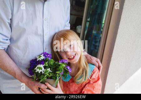 Fille souriante tenant une plante en pot par le père Banque D'Images