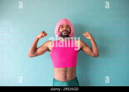 Jeune homme queer fléchissant les muscles debout devant le mur Banque D'Images