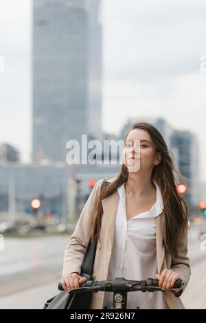 Femme d'affaires souriante debout avec un scooter électrique Banque D'Images