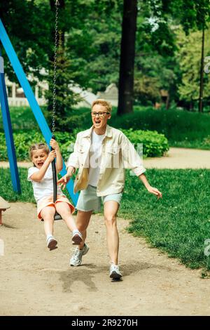 Mère gaie avec fille balançant sur balançoire à l'aire de jeux Banque D'Images