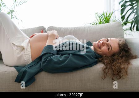Bonne femme enceinte se relaxant sur le canapé à la maison Banque D'Images