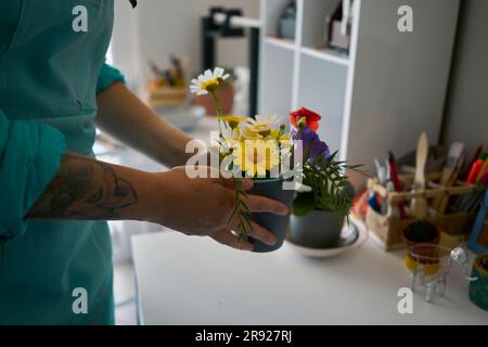 Femme organisant pot de fleurs sur table à l'atelier Banque D'Images