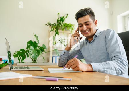 Homme d'affaires souriant parlant sur smartphone au bureau Banque D'Images