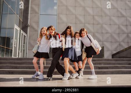 Des écolières heureuses se tenant debout devant le bâtiment de l'école Banque D'Images