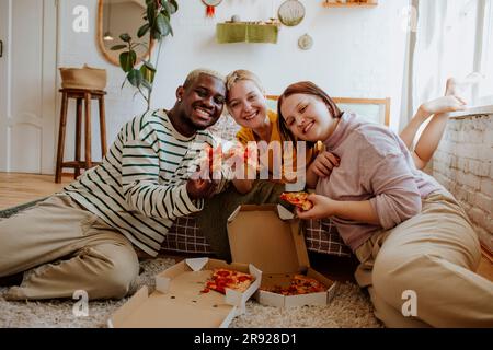 Jeunes amis souriants qui mangent de la pizza au lit Banque D'Images