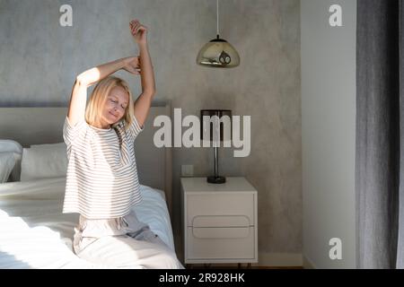 Femme étirant les bras avec les yeux fermés assis sur le lit Banque D'Images