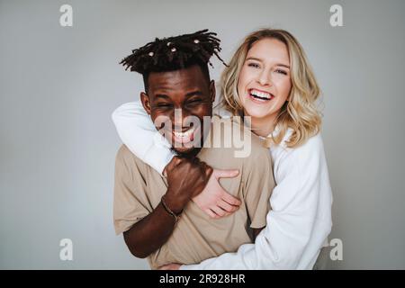 Jeune couple joyeux avec le bras autour de rire sur fond gris Banque D'Images