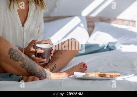 Femme assise au lit et prenant le petit déjeuner à la maison Banque D'Images