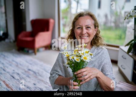 Femme âgée heureuse avec vase de fleurs à la maison Banque D'Images