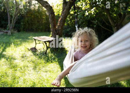 Bonne fille assise sur un hamac dans le jardin Banque D'Images