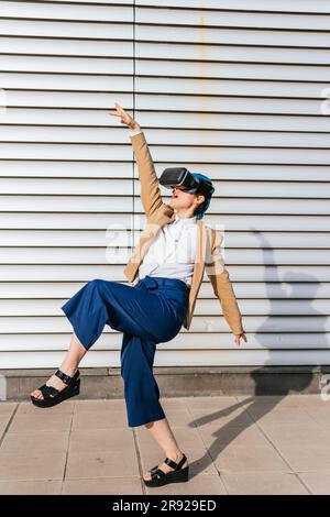 Femme d'affaires portant un casque de réalité virtuelle dansant devant le mur Banque D'Images